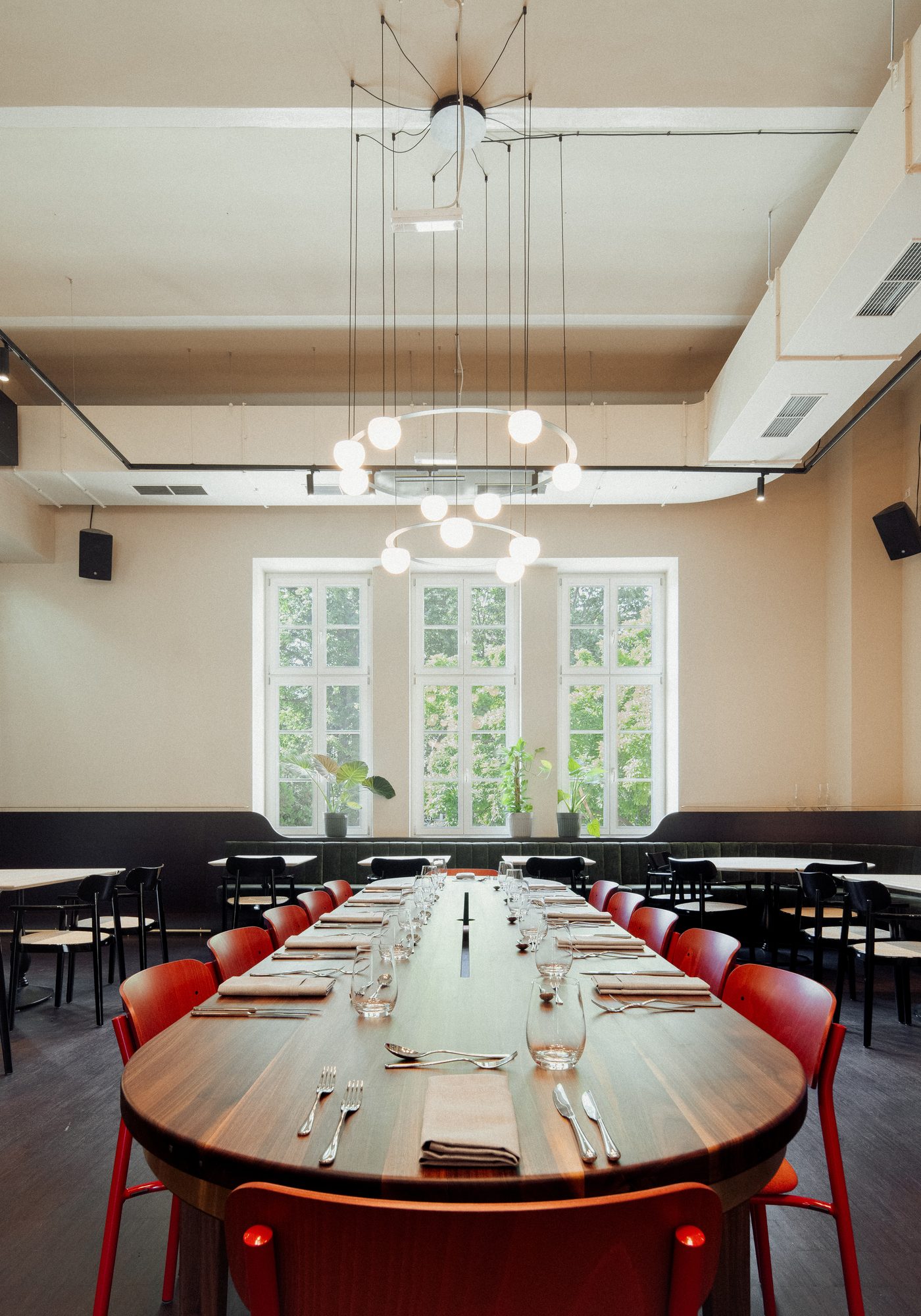 Community Table: lange Holztafel mit roten Stühlen vor den hohen Fenstern der sophie7
